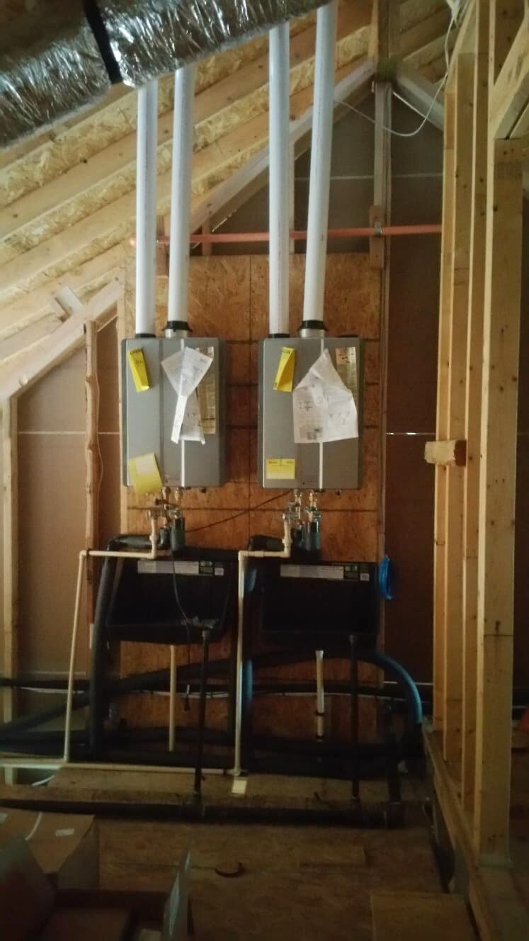 Two tankless water heaters installed side by side in an attic